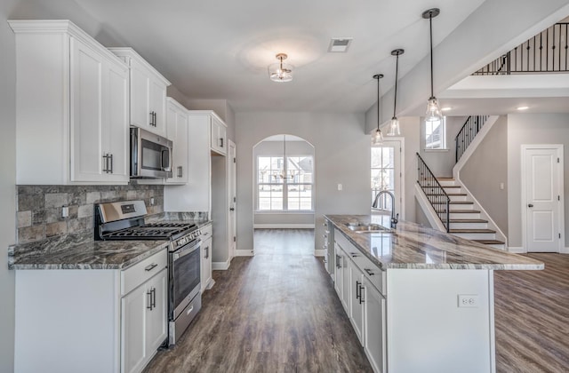 kitchen with decorative light fixtures, an island with sink, white cabinetry, sink, and stainless steel appliances