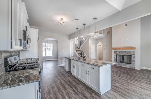 kitchen featuring pendant lighting, appliances with stainless steel finishes, dark stone countertops, white cabinets, and a stone fireplace