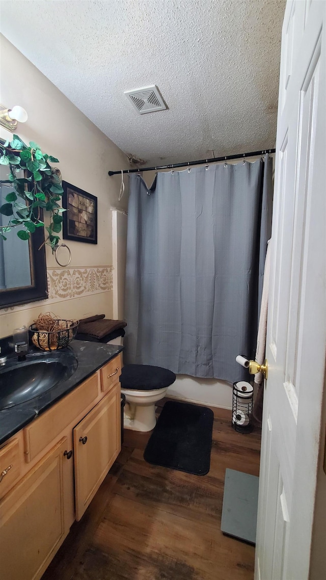 full bathroom with hardwood / wood-style flooring, vanity, toilet, shower / bath combo, and a textured ceiling