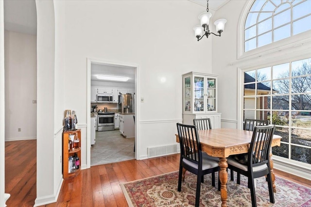 dining area with wood-type flooring, plenty of natural light, a towering ceiling, and an inviting chandelier