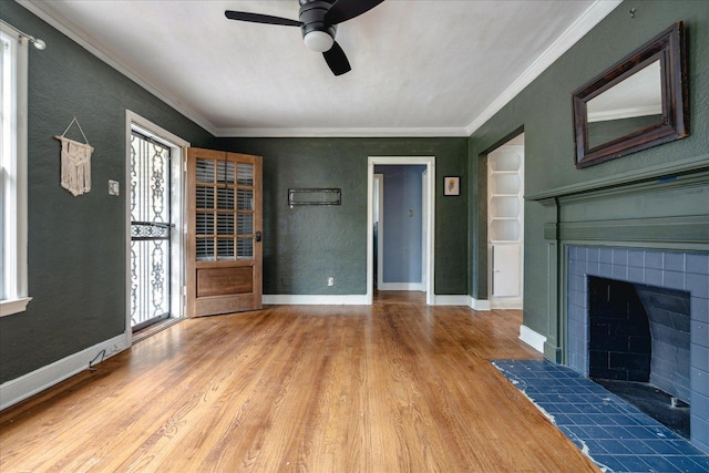 unfurnished living room with crown molding, ceiling fan, a tiled fireplace, and hardwood / wood-style floors