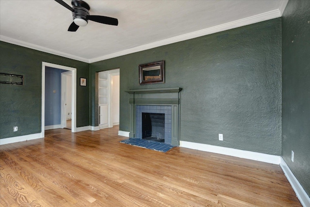 unfurnished living room with a tile fireplace, crown molding, ceiling fan, and light hardwood / wood-style flooring