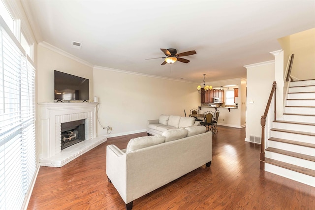 living room with crown molding, a brick fireplace, ceiling fan, and dark hardwood / wood-style flooring