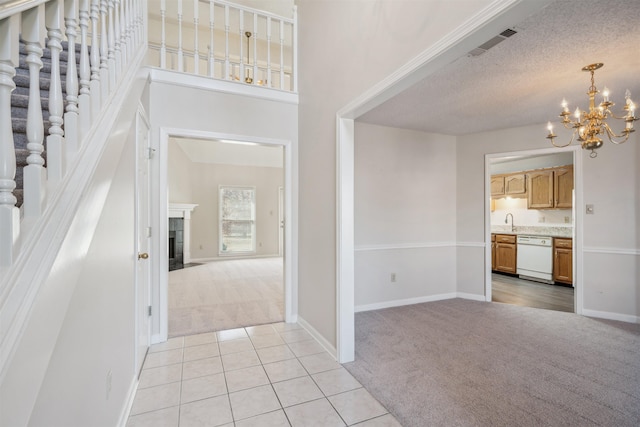 carpeted entryway featuring sink, an inviting chandelier, a textured ceiling, a towering ceiling, and a tiled fireplace