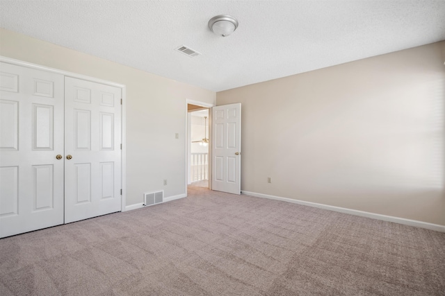 unfurnished bedroom featuring light colored carpet, a closet, and a textured ceiling