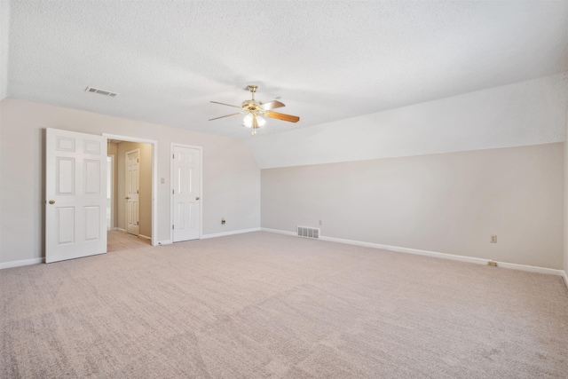 interior space featuring ceiling fan, lofted ceiling, light colored carpet, and a textured ceiling