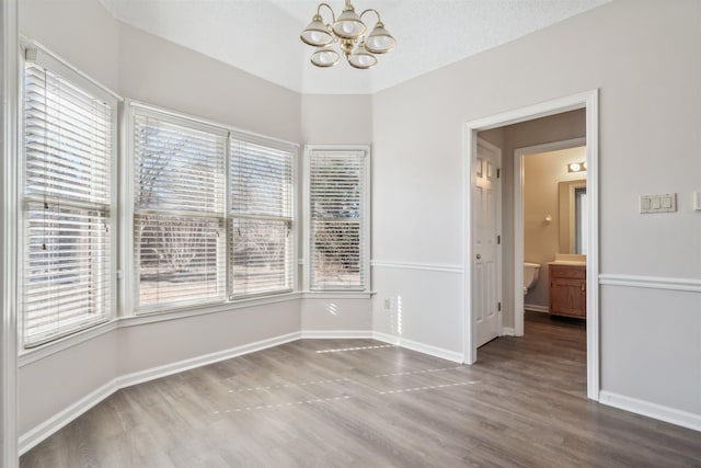 empty room featuring hardwood / wood-style flooring, a wealth of natural light, a textured ceiling, and an inviting chandelier