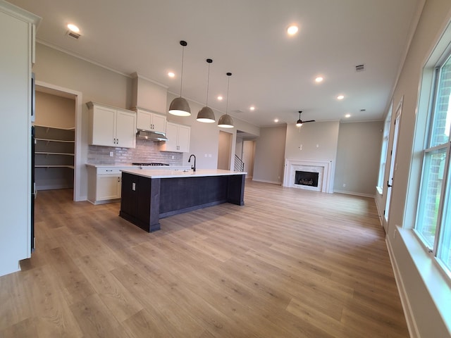 kitchen featuring a wealth of natural light, white cabinetry, an island with sink, hanging light fixtures, and ornamental molding