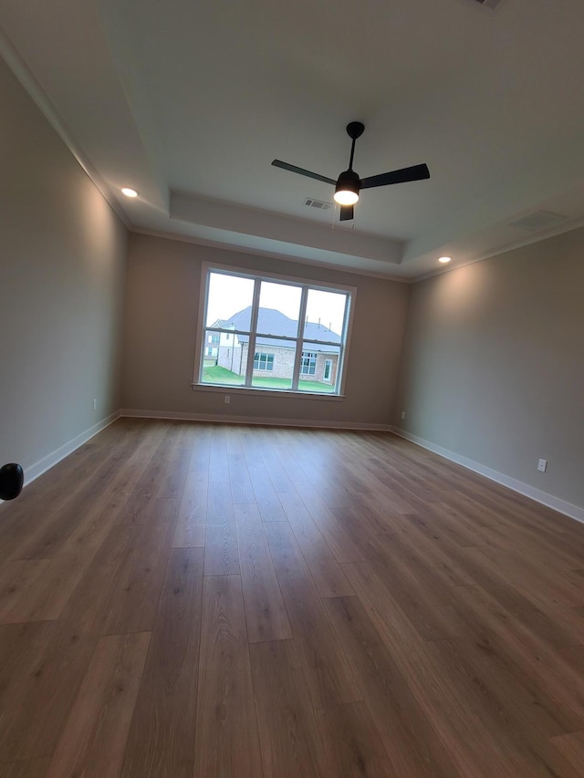 empty room featuring a raised ceiling, wood-type flooring, and ceiling fan