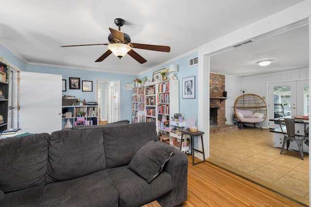 living room with ceiling fan, ornamental molding, light hardwood / wood-style floors, a brick fireplace, and french doors