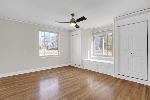 unfurnished bedroom featuring multiple windows, crown molding, wood-type flooring, and ceiling fan