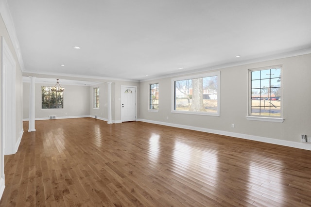 unfurnished living room featuring ornate columns, crown molding, and a chandelier