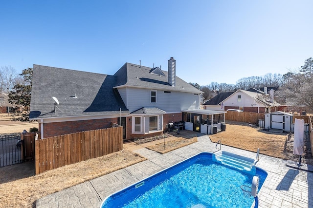 back of house with a fenced in pool, a patio area, a sunroom, and a storage unit