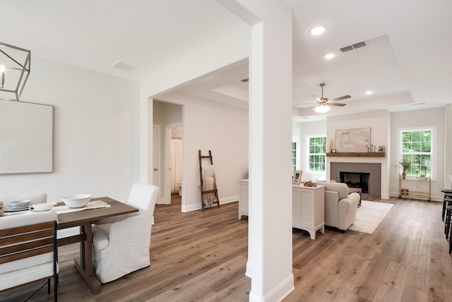 dining room featuring ceiling fan, a fireplace, light hardwood / wood-style floors, and a tray ceiling