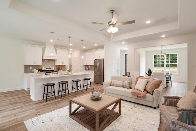 living room featuring sink, a tray ceiling, light hardwood / wood-style flooring, and ceiling fan