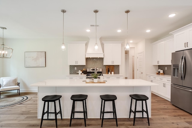 kitchen featuring white cabinetry, appliances with stainless steel finishes, hanging light fixtures, and a center island with sink