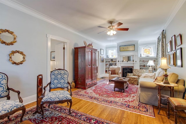 living room featuring a brick fireplace, crown molding, wood-type flooring, and ceiling fan