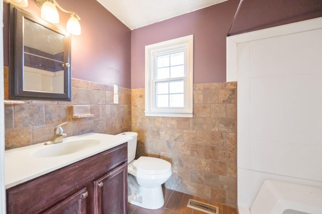 bathroom with vanity, toilet, tile walls, and a shower