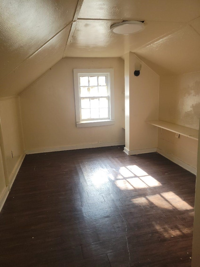 additional living space featuring dark hardwood / wood-style flooring, vaulted ceiling, and a textured ceiling