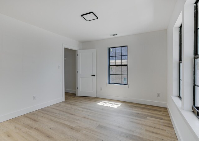 empty room with light wood-style floors, visible vents, and baseboards