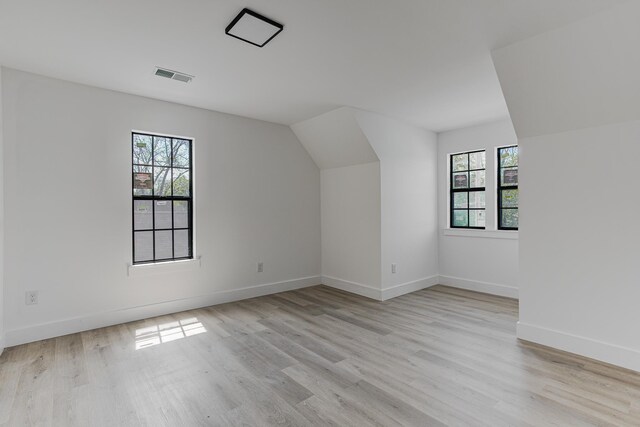 additional living space with baseboards, light wood finished floors, vaulted ceiling, and visible vents