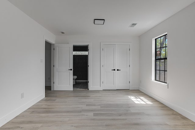 unfurnished bedroom featuring visible vents, ensuite bathroom, baseboards, and light wood-style floors