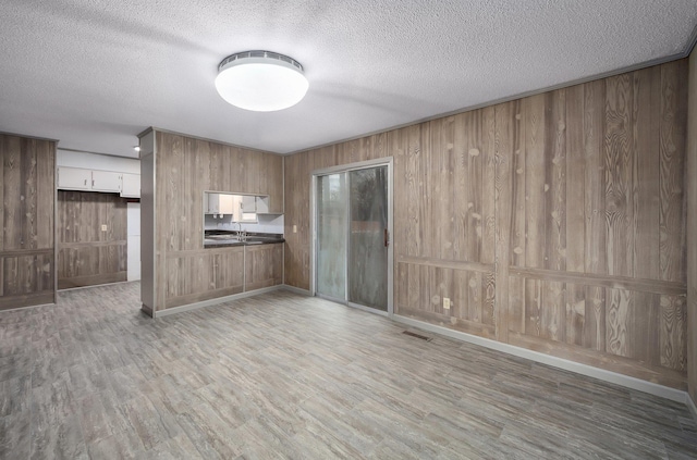 kitchen with white cabinetry, wooden walls, a textured ceiling, and light hardwood / wood-style flooring