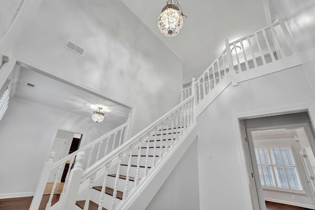 stairway with a notable chandelier, wood-type flooring, ornamental molding, and a high ceiling