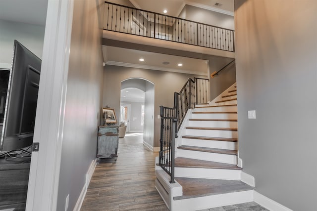 stairs with a towering ceiling, ornamental molding, and hardwood / wood-style floors