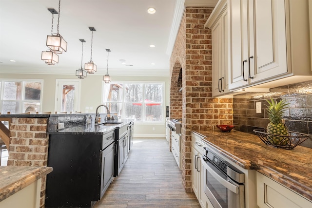 kitchen with sink, decorative light fixtures, dark stone countertops, oven, and cream cabinetry