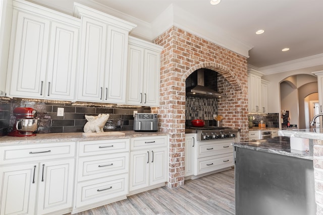 kitchen with wall chimney range hood, ornamental molding, light stone countertops, decorative backsplash, and stainless steel gas stovetop