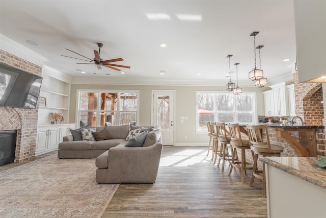 living room with ornamental molding, a brick fireplace, built in shelves, and light hardwood / wood-style flooring