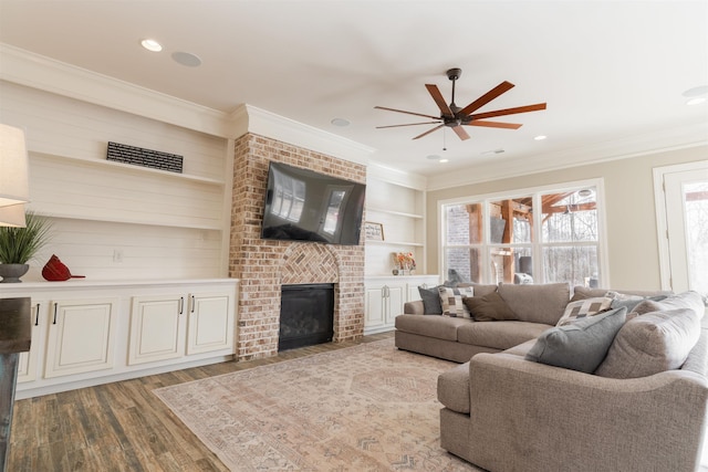 living room featuring ceiling fan, hardwood / wood-style floors, ornamental molding, a brick fireplace, and built in shelves