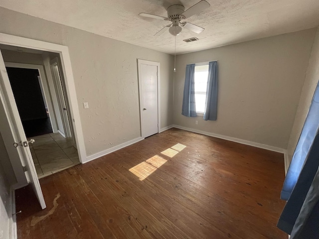 unfurnished bedroom featuring a closet, a textured ceiling, dark hardwood / wood-style floors, and ceiling fan