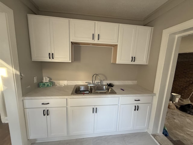 kitchen with brick wall, sink, a textured ceiling, and white cabinets