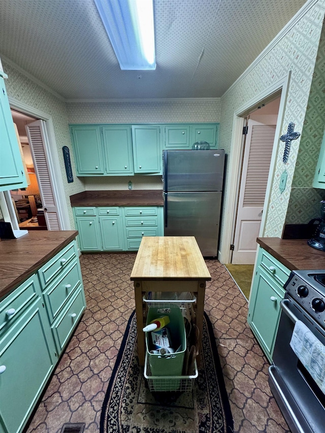 kitchen with range with electric cooktop, butcher block counters, stainless steel fridge, ornamental molding, and green cabinetry