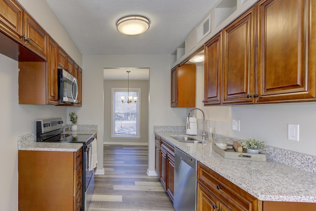 kitchen featuring sink, hanging light fixtures, light hardwood / wood-style floors, stainless steel appliances, and light stone countertops