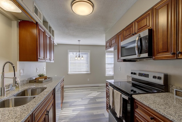 kitchen featuring pendant lighting, sink, appliances with stainless steel finishes, light stone countertops, and light wood-type flooring