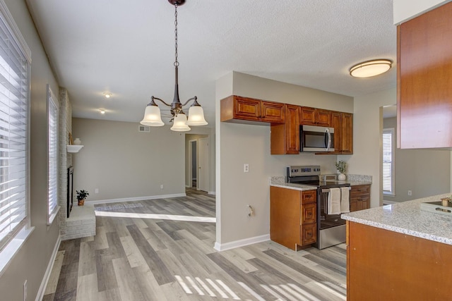 kitchen with a fireplace, decorative light fixtures, light hardwood / wood-style floors, stainless steel appliances, and light stone countertops