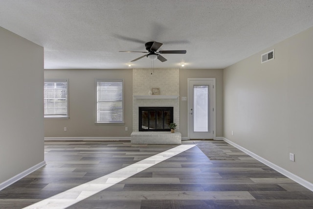 unfurnished living room with dark hardwood / wood-style flooring, a brick fireplace, a textured ceiling, and ceiling fan