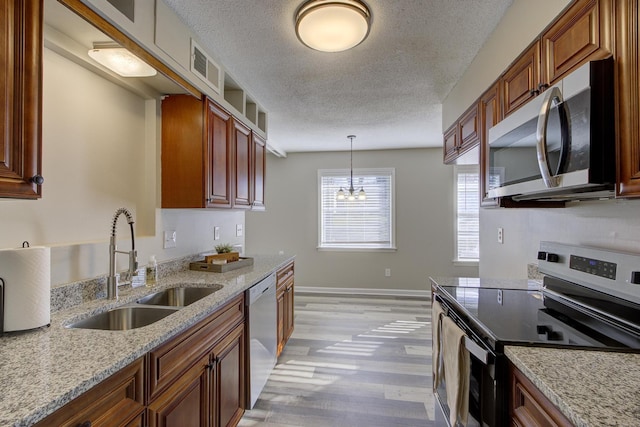 kitchen featuring sink, light stone counters, hanging light fixtures, light wood-type flooring, and stainless steel appliances