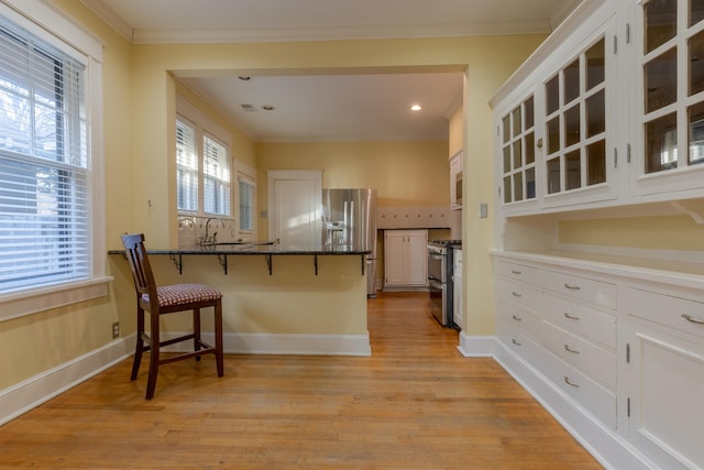 kitchen featuring appliances with stainless steel finishes, white cabinetry, a kitchen bar, kitchen peninsula, and crown molding