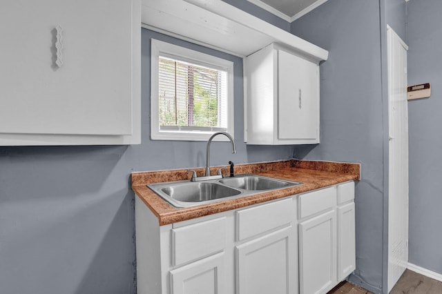 kitchen with sink, crown molding, white cabinets, and hardwood / wood-style flooring