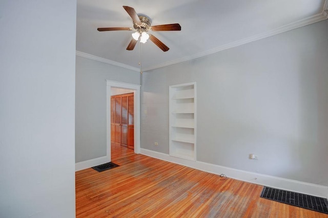 empty room with built in shelves, ceiling fan, crown molding, and light wood-type flooring