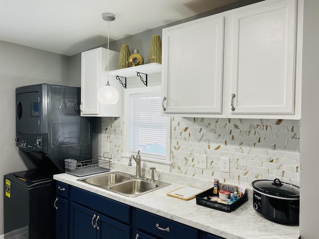 kitchen featuring blue cabinetry, stacked washer and clothes dryer, sink, white cabinetry, and backsplash