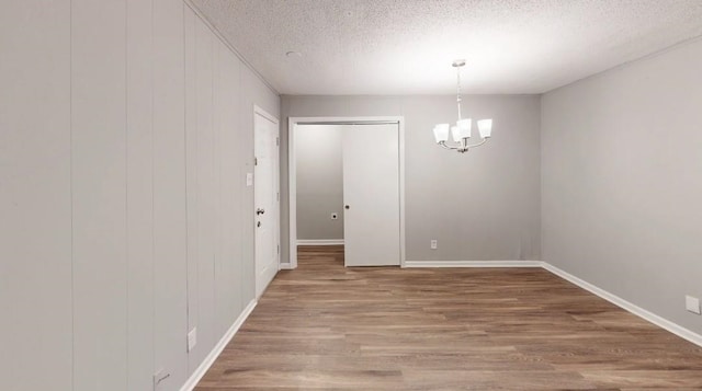 spare room featuring an inviting chandelier, wood-type flooring, and a textured ceiling