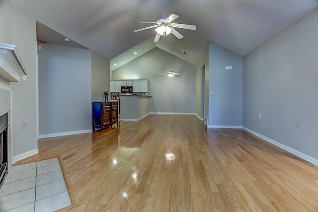 unfurnished living room featuring a tiled fireplace, lofted ceiling, light hardwood / wood-style floors, and ceiling fan