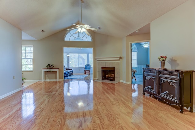 living room with vaulted ceiling, a tile fireplace, light hardwood / wood-style floors, and ceiling fan