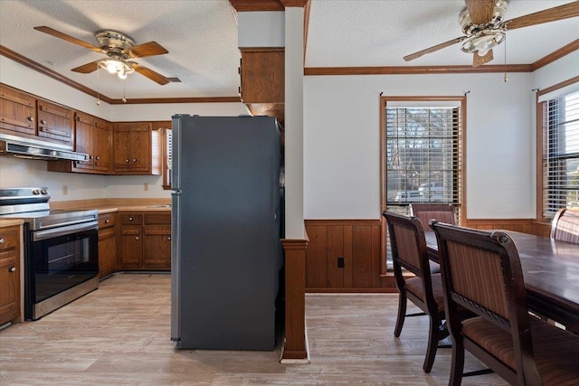 kitchen featuring stainless steel range with electric stovetop, crown molding, wood walls, and refrigerator