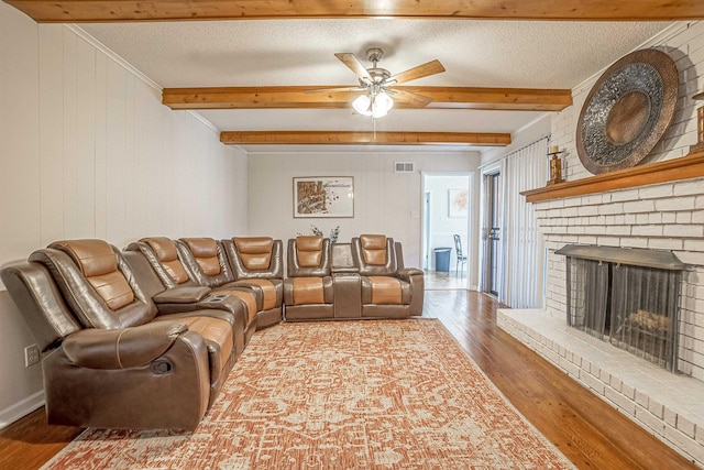 living room featuring ceiling fan, hardwood / wood-style floors, beam ceiling, a fireplace, and a textured ceiling